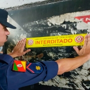 Na imagem, bombeiro militar fixa adesivo na parede escrito interditado.