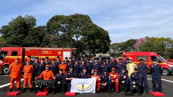 Formandos e Instrutores da 1 Edição do Curso de Operador em Salvamento Veicular reunidos, segurando a bandeira do curso, no pátio da formatura. 